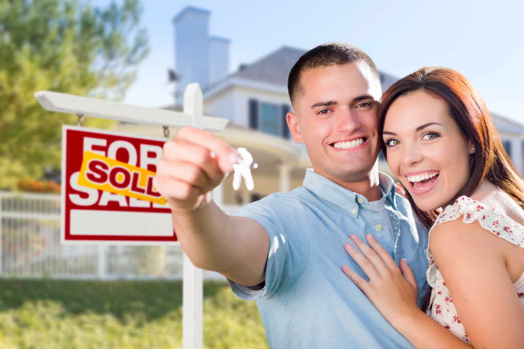 Mixed Race Excited Military Couple In Front of New Home with New House Keys and Sold Real Estate Sign Outside